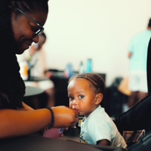 A woman in glasses feeding a baby in a high chair at Groovy Gratitude.