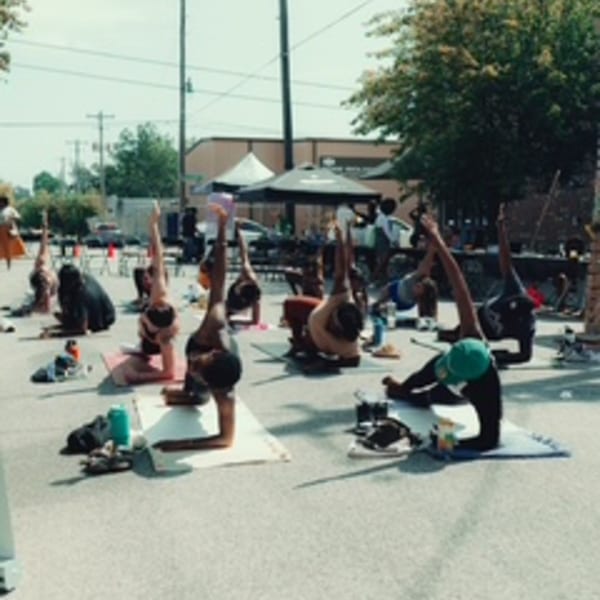 People doing yoga outdoors on mats, with buildings and trees in the background.