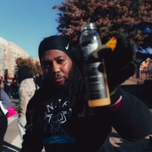 A man in a black beanie and hoodie holds out a Groovy Gratitude drink bottle.