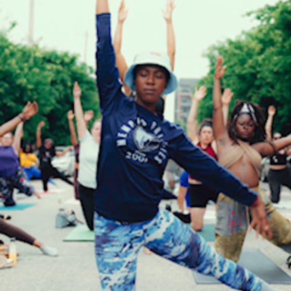 Diverse group of people doing outdoor yoga, stretching with arms raised, on a sunny day.