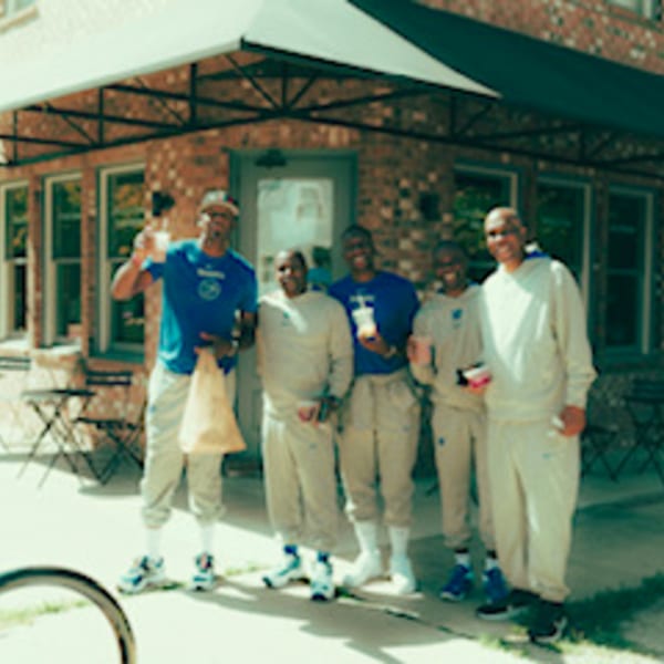 Five men in athletic wear stand outside Groovy Gratitude, holding drinks and a takeout bag.