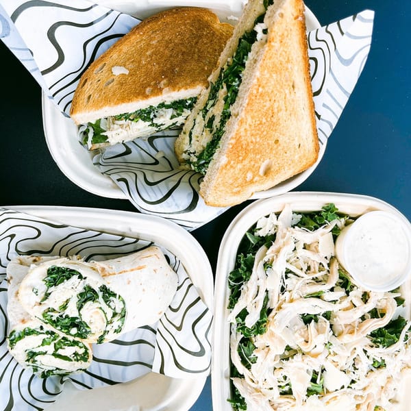 Groovy Gratitude's chicken sandwich, wrap, and salad with dressing, all in takeout containers.