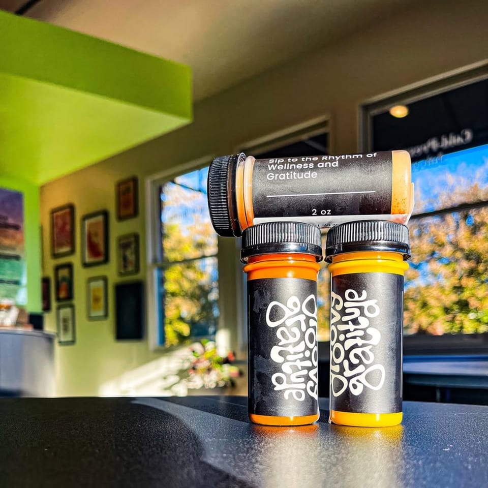 Three Groovy Gratitude wellness shots, two upright and one on its side, on a counter.