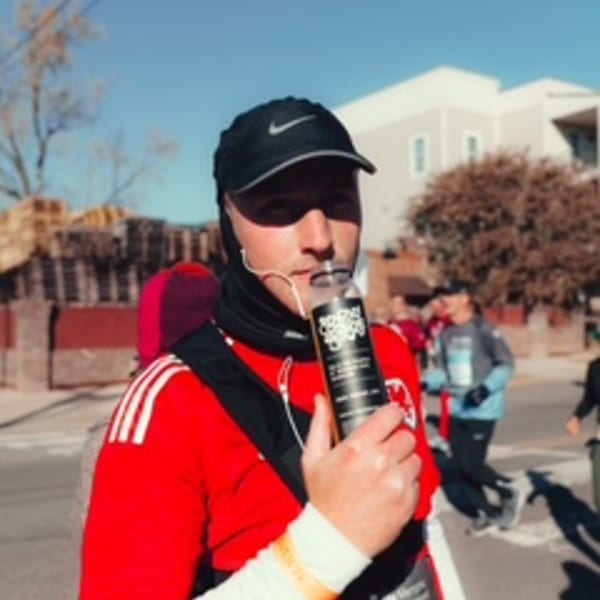 A man in a red shirt and black cap inhales from a portable oxygen canister on a sunny day.