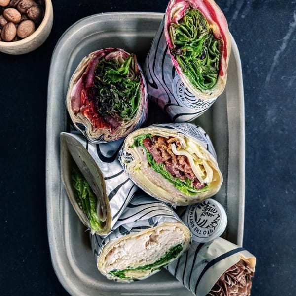 Assortment of Groovy Gratitude healthy wraps with various fillings, including bacon and chicken, in a gray tray.