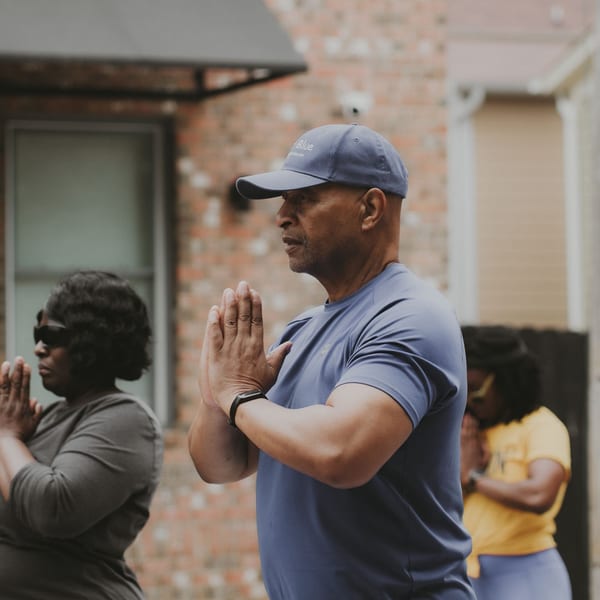 People in prayer pose during an outdoor yoga session, promoting Groovy Gratitude's healthy lifestyle.