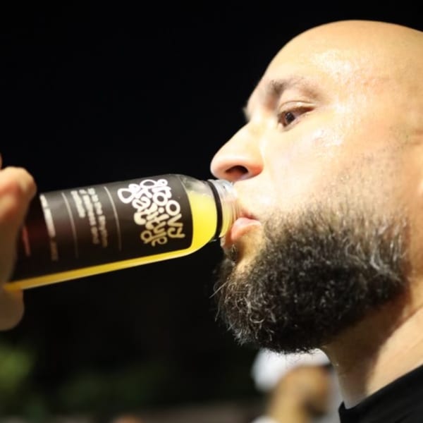 A man with a beard drinks a yellow Groovy Gratitude beverage from a black-labeled bottle.