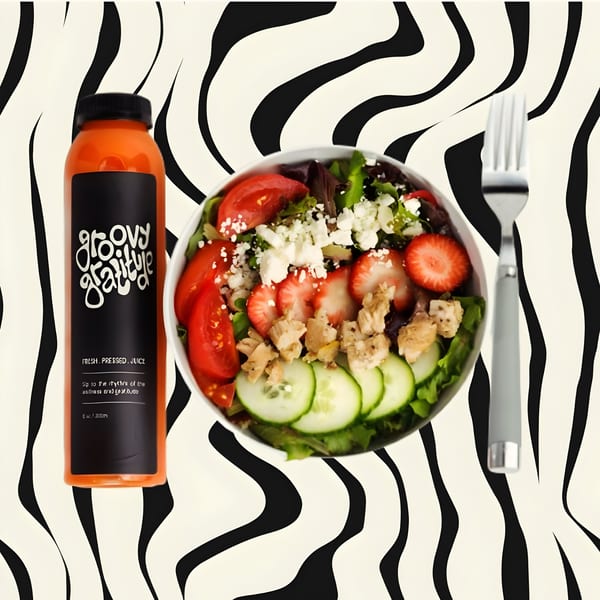 Groovy Gratitude juice bottle next to a fresh salad with chicken, strawberries, and feta.