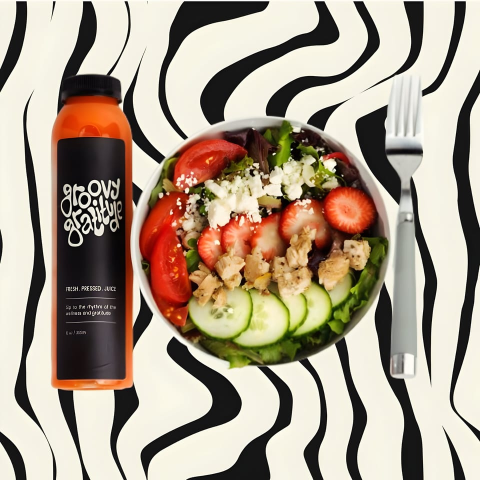 Groovy Gratitude juice bottle next to a fresh salad with chicken, strawberries, and feta.