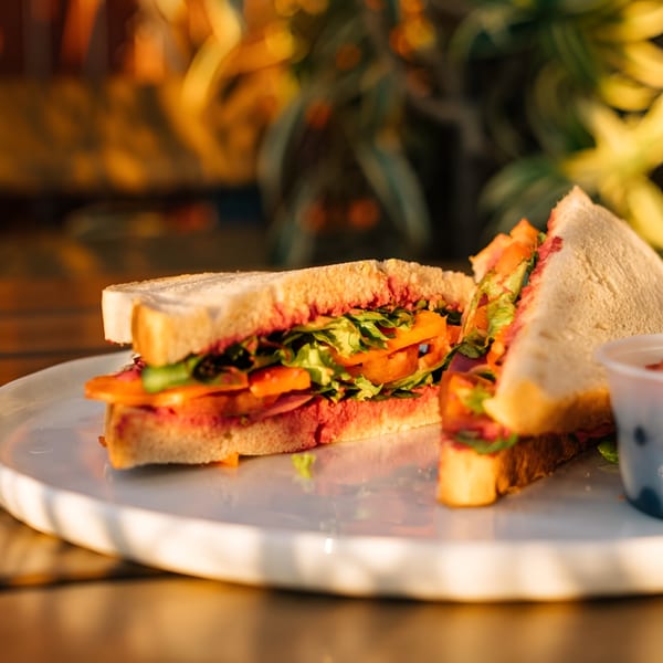 A healthy Groovy Gratitude sandwich with lettuce, tomatoes, and red spread on white bread.